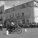 Fotografia da autoria de Américo Ribeiro, com o código de referência PT/AFAMR/FAR/NTR/04301, do Arquivo Municipal de Setúbal, que ilustra uma das inúmeras atividades realizadas pela FNAT, mostrando-se aqui uma gincana de motas realizada na Avenida Luísa Todi, no verão de 1956.